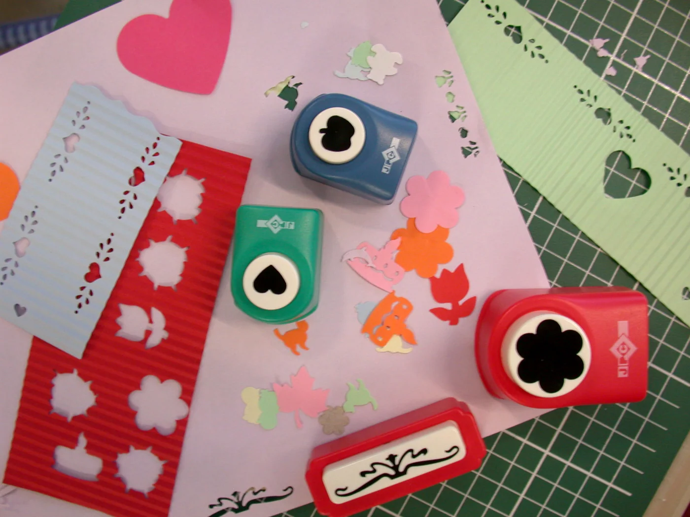 Craft punches cutting flower, heart, and border shapes from colourful corrugated papers.